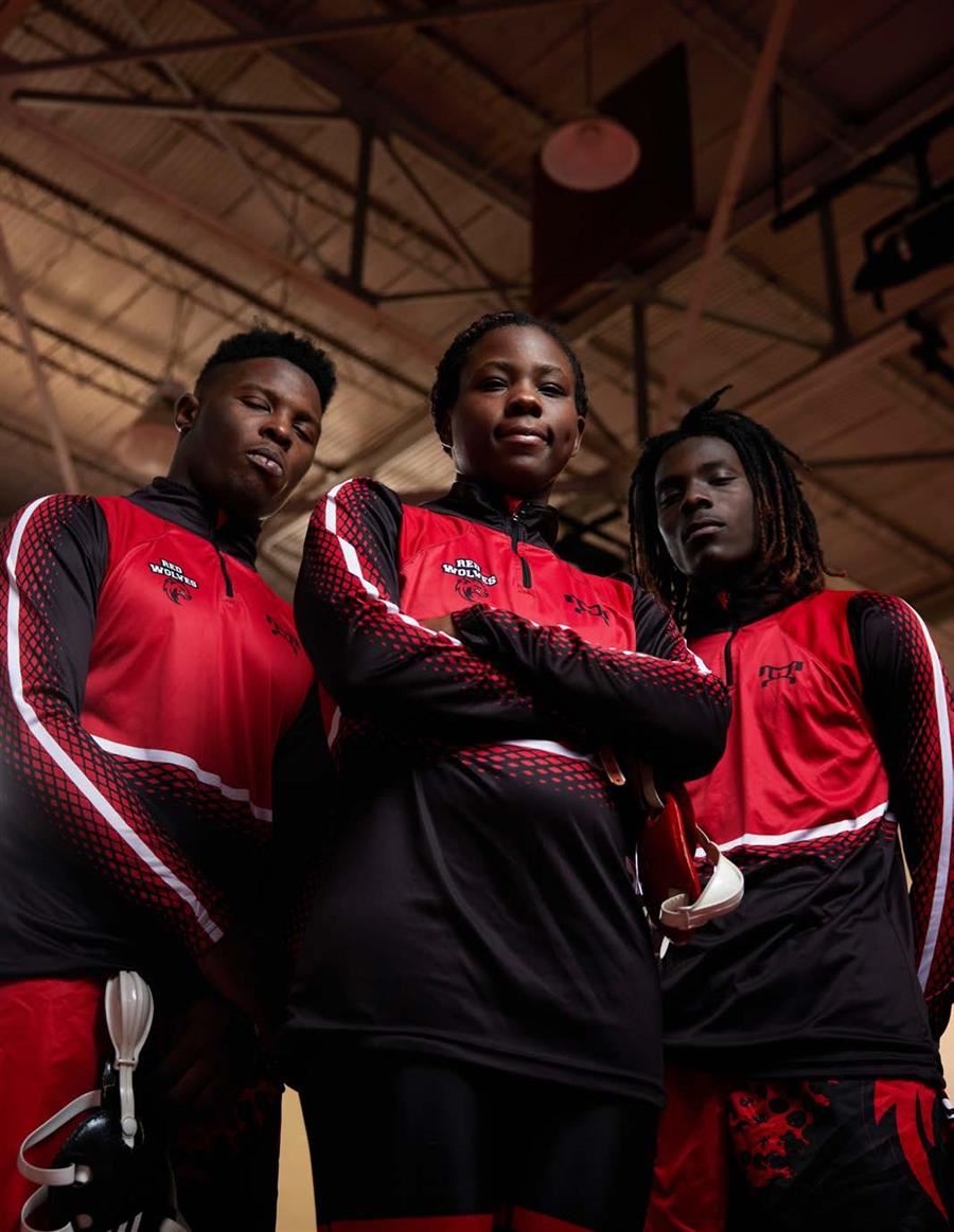 Three wrestlers in red and black "Red Wolves" uniforms stand confidently in a gym.